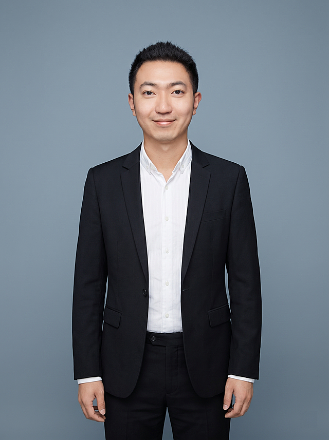 参考图中保留人物脸型、发型、年龄等特征生成网课讲师职场形象照，标准焦段50mm，f/4光圈，平视视角(镜头与人物视线齐平)；人物占画面70%，人物居中(居中构图)，位于画面中心，为视觉聚焦点，入境范围头部及以下至臀部下方10cm(半身像)；左右留少量背景空间；头部与画面顶部保留5%空间；头部发型完整，头肩比例协调，人物结构准确；发质微微柔顺，微微蓬松。身穿深黑色精纺羊毛混纺西装外套(平驳领设计，面料呈细腻微微哑光质感)；内搭白色高支精梳棉衬衫；下装深黑色精纺羊毛混纺西裤；着装正式干练；亲和专业，博学温润；身形匀称，姿态端正，身体挺拔。呈站姿，双手自然下垂，肢体放松且自信；简约冷蓝灰色纯色背景，呈现均匀柔和质感，背景光线均匀柔和，强化色彩对比的高级感，极简干净；画质超高分辨率、细节清晰，现代精致感风格；肤质精细化处理；眼神直视镜头，目光坚定且澄澈，表情自然。嘴角上扬；肤质自然细腻，肤色健康均匀，皮肤状态清爽干净，保留真实皮肤细节。正面柔光补光，4800K中性光，面部光比1:1.5。中近景写实摄影，对焦清晰，面部雾面柔光，轻透裸肌感，高清保留皮肤细节；分辨率4K，去除人物之外的所有元素。严格按照图片内容生成。画面比例3:4
