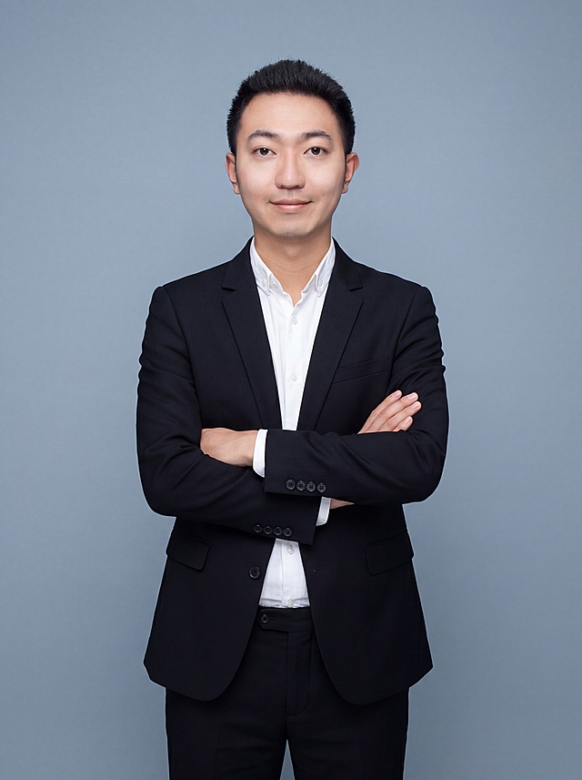 参考图中保留人物脸型、发型、年龄等特征生成网课讲师职场形象照，标准焦段50mm，f/4光圈，平视视角(镜头与人物视线齐平)；人物占画面70%，人物居中(居中构图)，位于画面中心，为视觉聚焦点，入境范围头部及以下至臀部下方10cm(半身像)；左右留少量背景空间；头部与画面顶部保留5%空间；头部发型完整，头肩比例协调，人物结构准确；发质微微柔顺，微微蓬松。身穿深黑色精纺羊毛混纺西装外套(平驳领设计，面料呈细腻微微哑光质感)；内搭白色高支精梳棉衬衫；下装深黑色精纺羊毛混纺西裤；着装正式干练；亲和专业，博学温润；身形匀称，姿态端正，身体挺拔。呈站姿，双手抱胸，肢体放松且自信；简约冷蓝灰色纯色背景，呈现均匀柔和质感，背景光线均匀柔和，强化色彩对比的高级感，极简干净；画质超高分辨率、细节清晰，现代精致感风格；肤质精细化处理；眼神直视镜头，目光坚定且澄澈，表情自然。嘴角上扬；肤质自然细腻，肤色健康均匀，皮肤状态清爽干净，保留真实皮肤细节。正面柔光补光，4800K中性光，面部光比1:1.5。中近景写实摄影，对焦清晰，面部雾面柔光，轻透裸肌感，高清保留皮肤细节；分辨率4K，去除人物之外的所有元素。严格按照图片内容生成。画面比例3:4