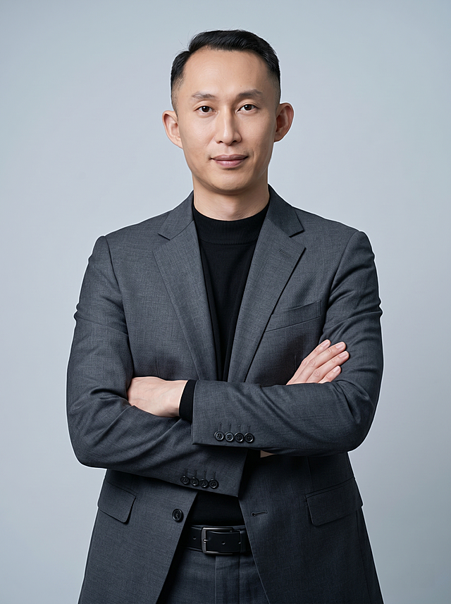 参考图中保留人物脸型、发型、年龄等特征生成职场形象照,标准焦段50mm,f/4光圈(f/2.8-f/4区间),平视视角(镜头与人物视线齐平);人物占画面70%,人物居中(居中构图),位于画面中心,为视觉聚焦点,入境范围头部及以下至臀部下方10cm(半身像);左右留少量背景空间;头部与画面顶部保留5%空间;头部发型完整,头肩比例协调,人物结构准确;身穿修身精纺羊毛混纺面料的深灰色西装外套(含5%桑蚕丝提升柔光质感),平驳领(商务感正式感),左胸袋无口袋巾(简化高级感),西装下摆自然垂度;内搭黑色中领紧身针织上衣,下装精纺羊毛混纺面料的深灰色高腰直筒西裤(面料同西装),搭配黑色哑光头层牛皮皮带(宽1.5cm),带扣为长方形拉丝黑色金属(1.8cm×2.5cm);着装正式干练;专业稳重;身形匀称,姿态端正,身体挺拔。呈正面抱胸的自然站立姿态:左臂搭于右臂上方,肩颈自然松弛下沉,姿态自信从容;发质微微柔顺，微微蓬松。简约冷调浅灰色纯色背景(呈现均匀柔和质感),背景光线均匀柔和,强化色彩对比的高级感。极简干净;画质超高分辨率、细节清晰,现代精致感风格;肤质精细化处理;眼神直视镜头,目光坚定且澄澈,表情自然。嘴角上扬;肤质自然细腻,肤色健康均匀,皮肤状态清爽干净,保留真实皮肤细节｡正面柔光补光,4800K中性光,面部光比1:1.5｡中近景写实摄影,对焦清晰,面部雾面柔光,轻透裸肌感,高清保留皮肤细节｡分辨率4K,去除人物之外的所有元素。严格按照图片内容生成。画面比例3:4