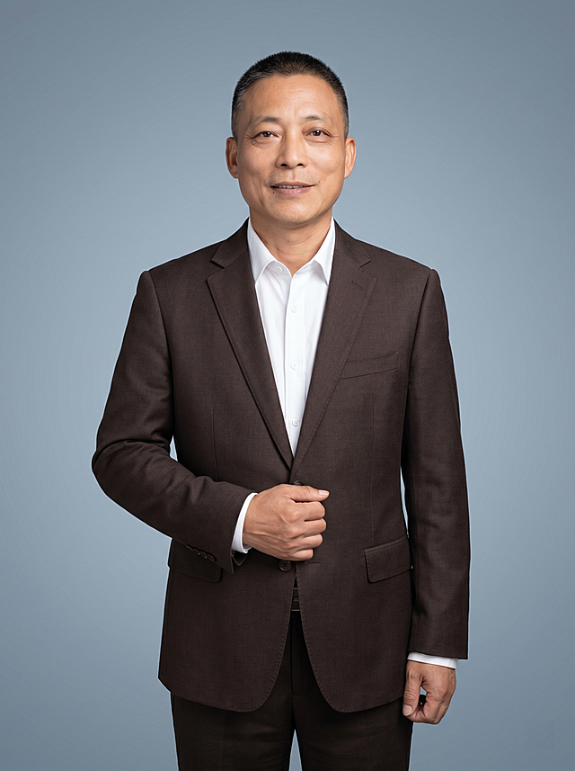 参考图中保留人物脸型、发型、年龄等特征生成金融保险行业职场形象照,标准焦段50mm,f/4光圈(f/2.8-f/4区间),平视视角(镜头与人物视线齐平);人物占画面70%,人物居中(居中构图),位于画面中心,为视觉聚焦点,入境范围头部及以下至臀部下方10cm(半身像);左右留少量背景空间;头部与画面顶部保留5%空间;头部发型完整,头肩比例协调,人物结构准确;发质微微柔顺，微微蓬松。身穿深棕色精纺羊毛混纺西装外套,(平驳领设计,面料呈细腻微微哑光质感);内搭白色高支棉衬衫;下装深棕色精纺羊毛混纺西裤;着装正式干练;专业稳重、精明专业、值得托付、稳重务实;身形匀称,姿态端正,身体挺拔。呈右手轻握西装前襟的自然姿态，肢体放松且自信;简约冷灰蓝纯色背景(呈现均匀柔和质感),背景光线均匀柔和,强化色彩对比的高级感。极简干净;画质超高分辨率、细节清晰,现代精致感风格;肤质精细化处理;眼神直视镜头,目光坚定且澄澈,表情自然。嘴角上扬;肤质自然细腻,肤色健康均匀,皮肤状态清爽干净,保留真实皮肤细节｡正面柔光补光,4800K中性光,面部光比1:1.5｡中近景写实摄影,对焦清晰,面部雾面柔光,轻透裸肌感,高清保留皮肤细节｡分辨率4K,去除人物之外的所有元素。严格按照图片内容生成。画面比例3:4
