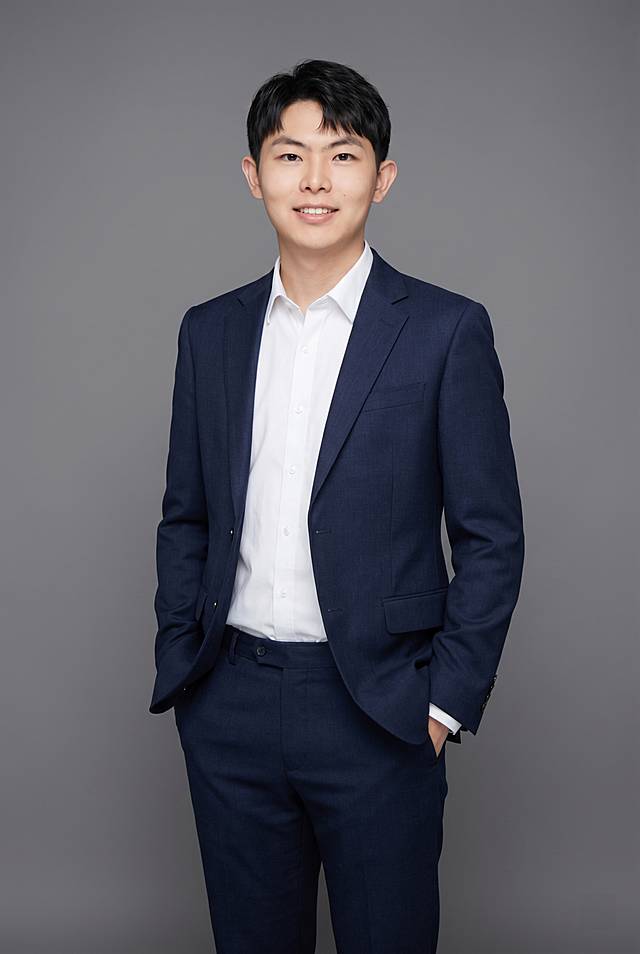 参考图中保留人物脸型、发型、年龄等特征，生成教师科研方向的正装全身形象照，标准焦段50mm,f/4光圈(f/2.8-f/4区间),平视视角(镜头与人物视线齐平);人物占画面主体，人物居中(居中构图),位于画面中心,为视觉聚焦点,全身照, 展现人物完整身形;左右留少量背景空间;头部与画面顶部保留5%空间;头部发型完整,头肩比例协调,人物结构准确;身穿深黑色精纺羊毛混纺西装外套,(平驳领设计,面料呈细腻微微哑光质感);内搭白色高支精梳棉衬衫;下装深黑色精纺羊毛混纺西裤;着装正式干练;博学温润、学者风范、从容儒雅、知性内敛;身形匀称,姿态端正,身体挺拔。呈站姿双手插兜的自然姿态，肢体放松且自信;发质微微柔顺，微微蓬松。简约微微中度灰色纯色背景(呈现均匀柔和质感),背景光线均匀柔和,强化色彩对比的高级感。极简干净;画质超高分辨率、细节清晰,现代精致感风格;肤质精细化处理;眼神直视镜头,目光坚定且澄澈,表情自然。嘴角上扬;肤质自然细腻,肤色健康均匀,皮肤状态清爽干净,保留真实皮肤细节｡正面柔光补光,4800K中性光,面部光比1:1.5｡写实摄影,对焦清晰,面部雾面柔光,轻透裸肌感,高清保留皮肤细节｡分辨率4K,去除人物之外的所有元素。严格按照图片内容生成。画面比例2:3