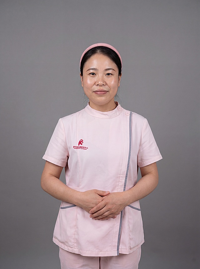 参考图中保留人物脸型、发型、年龄等特征生成医护职业形象照,标准焦段50mm,f/4光圈(f/2.8-f/4区间),平视视角(镜头与人物视线齐平);人物占画面70%,人物居中(居中构图),位于画面中心,为视觉聚焦点,入境范围头部及以下至臀部下方10cm(半身像);左右留少量背景空间;头部与画面顶部保留5%空间;头部发型完整,头肩比例协调,人物结构准确;身穿粉色医护工作服，保留灰色镶边和红色刺绣logo，面料干净整洁;下装同色医护裤;着装正式干练;专业可靠，温和严谨;身形匀称,姿态端正,身体挺拔。呈站姿，双手交叠于腹前的自然姿态，肢体放松且自信;保留发箍配饰;发质微微柔顺，微微蓬松。简约微微中度灰色纯色背景(呈现均匀柔和质感),背景光线均匀柔和,强化色彩对比的高级感。极简干净;画质超高分辨率、细节清晰,现代精致感风格;肤质精细化处理;眼神直视镜头,目光坚定且澄澈,表情自然。嘴角上扬;清透自然裸妆(轻薄底妆+淡唇妆)妆感轻薄轻透裸肌感,通透感肤质,肤质自然细腻,肤色健康均匀,雾面柔光裸肌感,保留真实皮肤细节｡正面柔光补光,4800K中性光,面部光比1:1.5,色调明亮｡中近景写实摄影,对焦清晰,高清保留皮肤细节｡分辨率4K,去除人物之外的所有元素。严格按照图片内容生成，画面比例3:4。