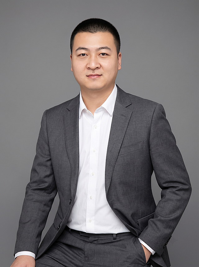 参考图中保留人物脸型、发型、年龄等特征生成职场形象照,标准焦段50mm,f/4光圈(f/2.8-f/4区间),平视视角(镜头与人物视线齐平);人物占画面70%,人物居中(居中构图),位于画面中心,为视觉聚焦点,入境范围头部及以下至臀部下方10cm(半身像);左右留少量背景空间;头部与画面顶部保留5%空间;头部发型完整,头肩比例协调,人物结构准确;发质微微柔顺，微微蓬松。身穿深灰色精纺羊毛混纺西装外套,(平驳领设计,面料呈细腻微微哑光质感);内搭白色高支精梳棉衬衫;下装深灰色精纺羊毛混纺西裤;着装正式干练;专业稳重;身形匀称,姿态端正,身体挺拔。呈坐姿，单手插兜的自然姿态，肢体放松且自信;简约微微中度灰色纯色背景(呈现均匀柔和质感),背景光线均匀柔和,强化色彩对比的高级感。极简干净;画质超高分辨率、细节清晰,现代精致感风格;肤质精细化处理;眼神直视镜头,目光坚定且澄澈,表情自然。嘴角上扬;肤质自然细腻,肤色健康均匀,皮肤状态清爽干净,保留真实皮肤细节｡正面柔光补光,4800K中性光,面部光比1:1.5｡中近景写实摄影,对焦清晰,面部雾面柔光,轻透裸肌感,高清保留皮肤细节｡分辨率4K,去除人物之外的所有元素。严格按照图片内容生成，适当美化颜值，画面比例3:4