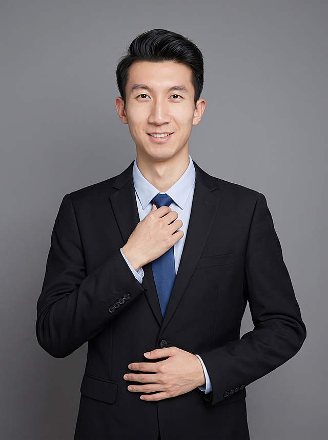 参考图中保留人物脸型、发型、年龄等特征生成职场形象照,标准焦段50mm,f/4光圈(f/2.8-f/4区间),平视视角(镜头与人物视线齐平);人物占画面70%,人物居中(居中构图),位于画面中心,为视觉聚焦点,入境范围头部及以下至臀部下方10cm(半身像);左右留少量背景空间;头部与画面顶部保留5%空间;头部发型完整,头肩比例协调,人物结构准确;发质微微柔顺，微微蓬松。身穿深黑色精纺羊毛混纺西装外套,(平驳领设计,面料呈细腻微微哑光质感);内搭浅蓝色衬衫;下装深黑色精纺羊毛混纺西裤;着装正式干练;专业稳重;身形匀称,姿态端正,身体挺拔。呈站立姿势，单手捏领带，另一只手摸腹部，肢体放松且自信;简约微微中度灰色纯色背景(呈现均匀柔和质感),背景光线均匀柔和,强化色彩对比的高级感。极简干净;画质超高分辨率、细节清晰,现代精致感风格;肤质精细化处理;眼神直视镜头,目光坚定且澄澈,表情自然。嘴角上扬;肤质自然细腻,肤色健康均匀,皮肤状态清爽干净,保留真实皮肤细节｡正面柔光补光,4800K中性光,面部光比1:1.5｡中近景写实摄影,对焦清晰,面部雾面柔光,轻透裸肌感,高清保留皮肤细节;分辨率4K,去除人物之外的所有元素。严格按照图片内容生成。画面比例3:4