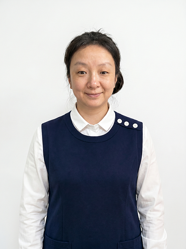 参考图中保留人物脸型、发型、年龄等特征生成育儿嫂形象照，标准焦段50mm,f/4光圈(f/2.8-f/4区间),平视视角(镜头与人物视线齐平);人物占画面70%,人物居中(居中构图),位于画面中心,为视觉聚焦点,入境范围头部及以下至臀部下方10cm(半身像);左右留少量背景空间;头部与画面顶部保留5%空间;头部发型完整,头肩比例协调,人物结构准确;身穿藏青色棉质无袖背心，内搭白色高支精梳棉衬衫；着装干净干练，亲和温暖有爱心，身形匀称,姿态端正,身体挺拔。呈自然站姿，肢体放松且自信;发质微微柔顺，微微蓬松。主体锐利,白色纯色背景，背景光线均匀柔和，强化色彩对比的高级感，极简干净;画质超高分辨率、细节清晰,现代精致感风格;肤质精细化处理;眼神直视镜头,目光坚定且澄澈,表情自然。嘴角上扬;清透自然裸妆(轻薄底妆+淡唇妆)妆感轻薄轻透裸肌感,通透感肤质,肤质自然细腻,肤色健康均匀,雾面柔光裸肌感,保留真实皮肤细节｡正面柔光补光,4800K中性光,面部光比1:1.5,色调明亮｡中近景写实摄影,对焦清晰,高清保留皮肤细节。分辨率4K,去除人物之外的所有元素。严格按照图片内容生成，画面比例3:4。