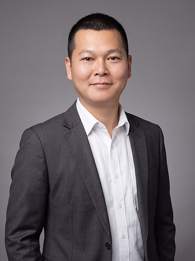 参考图中保留人物脸型、发型、年龄等特征生成金融行业职场形象照，标准焦段50mm，f/4光圈(f/2.8-f/4区间)，平视视角(镜头与人物视线齐平)；人物占画面70%，人物居中(居中构图)，位于画面中心，为视觉聚焦点，入境范围头部及以下至臀部下方10cm(半身像)；左右留少量背景空间；头部与画面顶部保留5%空间；头部发型完整，头肩比例协调，人物结构准确；发质微微柔顺，微微蓬松。身穿深灰色精纺羊毛混纺西装外套(平驳领设计，面料呈细腻微微哑光质感)；内搭白色高支精梳棉衬衫；下装深灰色精纺羊毛混纺西裤；着装正式干练；专业稳重，值得信赖；身形匀称，姿态端正，身体挺拔。呈自然站姿，双手自然下垂，肢体放松且自信；简约微微中度灰色纯色背景(呈现均匀柔和质感)，背景光线均匀柔和，强化色彩对比的高级感，极简干净。画质超高分辨率、细节清晰，现代精致感风格；肤质精细化处理；眼神直视镜头，目光坚定且澄澈，表情自然。嘴角上扬；肤质自然细腻，肤色健康均匀，皮肤状态清爽干净，保留真实皮肤细节。正面柔光补光，4800K中性光，面部光比1:1.5。中近景写实摄影，对焦清晰，面部雾面柔光，轻透裸肌感，高清保留皮肤细节。分辨率4K，去除人物之外的所有元素。去除所有配饰。严格按照图片内容生成。画面比例3:4