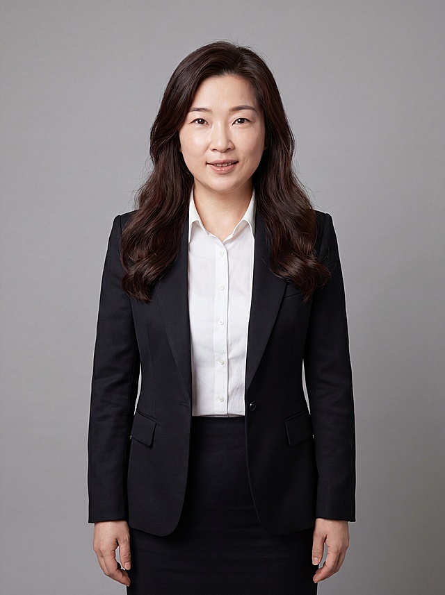 参考图中保留人物脸型、发型、年龄等特征生成通用职场形象照，标准焦段50mm，f/4光圈，平视视角，镜头与人物视线齐平；人物占画面70%，人物居中，居中构图，位于画面中心，为视觉聚焦点，入境范围头部及以下至臀部下方10cm，半身像；左右留少量背景空间；头部与画面顶部保留5%空间；头部发型完整，头肩比例协调，人物结构准确；发质微微柔顺，微微蓬松。身穿深黑色精纺羊毛混纺西装外套，平驳领设计，面料呈细腻微微哑光质感；内搭白色高支精梳棉衬衫；下装深黑色精纺羊毛混纺西装套裙；着装正式干练；专业稳重；身形匀称，姿态端正，身体挺拔。呈站姿，双臂自然下垂，肢体放松且自信；去除耳环配饰；简约微微中性灰色纯色背景，呈现均匀柔和质感，背景光线均匀柔和，强化色彩对比的高级感，极简干净；画质超高分辨率、细节清晰，现代精致感风格；肤质精细化处理；眼神直视镜头，目光坚定且澄澈，表情自然。嘴角上扬；清透自然裸妆，轻薄底妆+淡唇妆，妆感轻薄轻透裸肌感，通透感肤质，肤质自然细腻，肤色健康均匀，雾面柔光裸肌感，保留真实皮肤细节。正面柔光补光，4800K中性光，面部光比1:1.5，色调明亮。中近景写实摄影，对焦清晰，高清保留皮肤细节；分辨率4K，去除人物之外的所有元素。严格按照图片内容生成，画面比例3:4