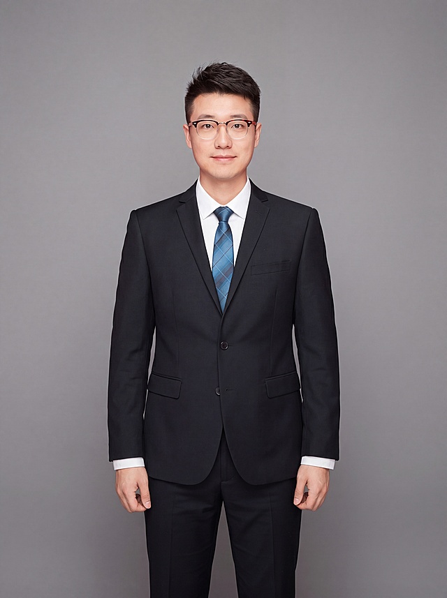 参考图中保留人物脸型、发型、年龄等特征生成职场形象照，标准焦段50mm，f/4光圈，平视视角，镜头与人物视线齐平；人物占画面，人物居中，居中构图，位于画面中心，为视觉聚焦点，全身照，展现人物完整身形；左右留少量背景空间；头部与画面顶部保留5%空间；头部发型完整，头肩比例协调，人物结构准确；身穿深黑色精纺羊毛混纺西装外套，平驳领设计，面料呈细腻微微哑光质感；内搭白色高支精梳棉衬衫；下装深黑色精纺羊毛混纺西裤；佩戴蓝色格纹领带，保留眼镜配饰；着装正式干练；专业稳重；身形匀称，姿态端正，身体挺拔。呈站立姿势，双臂自然垂直，肢体放松且自信；发质微微柔顺，微微蓬松；简约中性灰纯色背景，呈现均匀柔和质感，背景光线均匀柔和，强化色彩对比的高级感，极简干净；画质超高分辨率、细节清晰，现代精致感风格；肤质精细化处理；眼神直视镜头，目光坚定且澄澈，表情自然。嘴角上扬；肤质自然细腻，肤色健康均匀，哑光肤质清爽干净，保留真实皮肤细节；杰作，最佳画质，超高细节，写实摄影，全身人像，皮肤质感自然清晰，柔光，正面补光，画面干净清新，高清皮肤细节；面部光比1:1.5，4800K中性光，微微修饰脸型，肤质哑光细腻，面部雾面柔光，轻透裸肌感，真实毛孔纹理；分辨率4K，去除人物之外的所有元素，严格按照图片内容生成，画面比例3:4