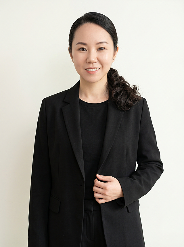 参考图中保留人物脸型、脸部完全沿用原图无任何改动，严格保留原图原生发型，不更改款式、不调整蓬松度、不换发型生成培训机构名师职场形象照，标准焦段50mm,f/4光圈(f/2.8-f/4区间),平视视角(镜头与人物视线齐平);人物占画面70%,人物居中(居中构图),位于画面中心,为视觉聚焦点,入境范围头部及以下至臀部下方10cm(半身像);左右留少量背景空间;头部与画面顶部保留5%空间;头部发型完整,头肩比例协调,人物结构准确;发质微微柔顺，微微蓬松。身穿落肩宽松黑色精纺羊毛混纺休闲西装外套,(平驳领设计,面料呈细腻微微哑光质感);内搭纯色高支精梳棉打底衫;下装同材质同黑色休闲西裤;着装正式干练;温柔亲和,身形匀称,姿态端正,身体挺拔。呈自然站姿，右手轻握西装前襟，肢体放松且自信;米白纯色墙面背景，正面均匀漫射柔光，光线平整柔和，无特殊光影氛围,呈现均匀柔和质感,极简干净;画质超高分辨率、细节清晰,现代精致感风格;画质修复高清锐化，肤质精细化处理;眼神直视镜头,目光坚定且澄澈,表情自然。嘴角上扬;清透自然裸妆(轻薄底妆+淡唇妆)妆感轻薄轻透裸肌感,通透感肤质,肤质自然细腻,肤色健康均匀,雾面柔光裸肌感,保留真实皮肤细节｡正面柔光补光,4800K中性光,面部光比1:1.5,色调明亮｡中近景写实摄影,对焦清晰,高清保留皮肤细节。分辨率4K,去除人物之外的所有元素。严格按照图片内容生成，培训机构名师商用半身人像，画面比例3:4
