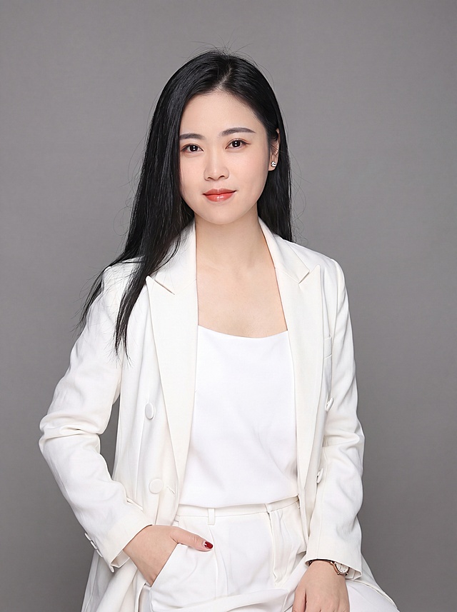 参考图中保留人物脸型、发型、年龄等特征生成职场形象照,标准焦段50mm,f/4光圈(f/2.8-f/4区间),平视视角(镜头与人物视线齐平);人物占画面70%,人物居中(居中构图),位于画面中心,为视觉聚焦点,含腿部半身照;左右留少量背景空间;头部与画面顶部保留5%空间;头部发型完整,头肩比例协调,人物结构准确;保留原图服装风格，着装正式干练;专业稳重;身形匀称,姿态端正,身体挺拔。呈自然坐姿，左手插兜，肢体放松且自信;发质微微柔顺，微微蓬松。佩戴精致配饰，简约微微中性灰色纯色背景(呈现均匀柔和质感),背景光线均匀柔和,强化色彩对比的高级感。极简干净;画质超高分辨率、细节清晰,现代精致感风格;肤质精细化处理;眼神直视镜头,目光坚定且澄澈,表情自然。嘴角上扬;清透自然裸妆(轻薄底妆+淡唇妆)妆感轻薄轻透裸肌感,通透感肤质,肤质自然细腻,肤色健康均匀,雾面柔光裸肌感,保留真实皮肤细节｡正面柔光补光,4800K中性光,面部光比1:1.5,色调明亮｡中近景写实摄影,对焦清晰,高清保留皮肤细节｡分辨率4K,去除人物之外的所有元素。严格按照图片内容生成。画面比例3:4
