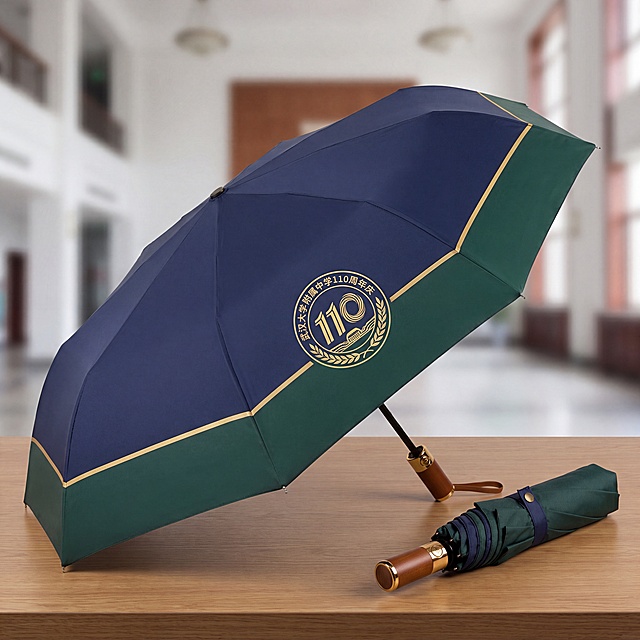 武汉大学附属中学110周年庆雨伞效果图，伞面印有提取的110周年庆徽章图案，配色深蓝绿配金色，折叠伞展示，图案清晰，无错别字，无扭曲模糊