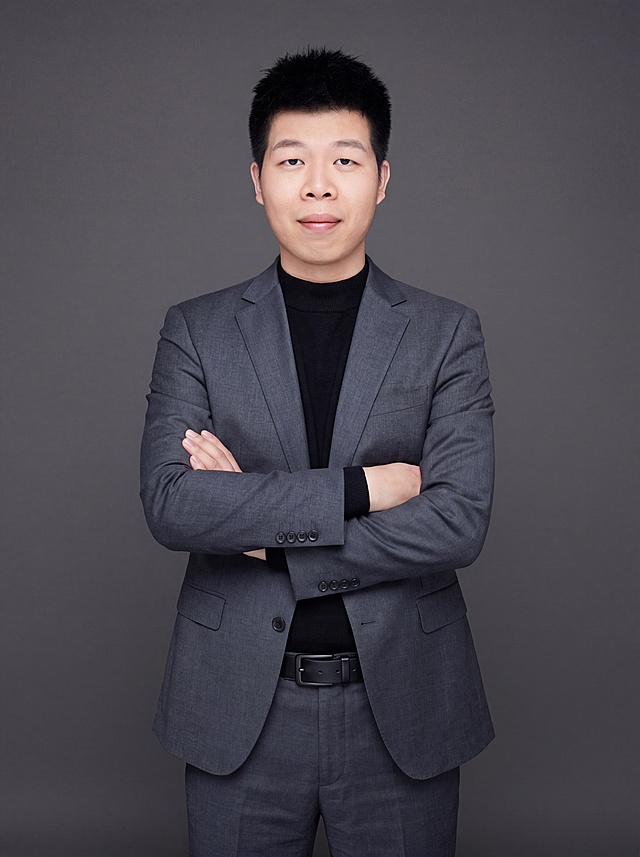 参考图中保留人物脸型、发型、年龄等特征生成职场形象照,标准焦段50mm,f/4光圈(f/2.8-f/4区间),平视视角(镜头与人物视线齐平);人物占画面70%,人物居中(居中构图),位于画面中心,为视觉聚焦点,入境范围头部及以下至臀部下方10cm(半身像);左右留少量背景空间;头部与画面顶部保留5%空间;头部发型完整,头肩比例协调,人物结构准确;身穿修身精纺羊毛混纺面料的深灰色西装外套(含5%桑蚕丝提升柔光质感),平驳领(商务感正式感),左胸袋无口袋巾(简化高级感),西装下摆自然垂度;内搭黑色中领紧身针织上衣,下装精纺羊毛混纺面料的深灰色高腰直筒西裤(面料同西装),搭配黑色哑光头层牛皮皮带(宽1.5cm),带扣为长方形拉丝黑色金属(1.8cm×2.5cm);着装正式干练;正式严谨专业稳重;身形匀称,姿态端正,身体挺拔。呈正面抱胸的自然站立姿态:左臂搭于右臂上方,肩颈自然松弛下沉,姿态自信从容;发质微微柔顺，微微蓬松。简约冷调深灰色纯色背景(呈现均匀柔和质感),背景光线均匀柔和,强化色彩对比的高级感。极简干净;画质超高分辨率、细节清晰,现代精致感风格;肤质精细化处理;眼神直视镜头,目光坚定且澄澈,表情自然。嘴角上扬;肤质自然细腻,肤色健康均匀,皮肤状态清爽干净,保留真实皮肤细节｡正面柔光补光,4800K中性光,面部光比1:1.5｡中近景写实摄影,对焦清晰,面部雾面柔光,轻透裸肌感,高清保留皮肤细节｡分辨率4K,去除人物之外的所有元素。严格按照图片内容生成。画面比例3:4
