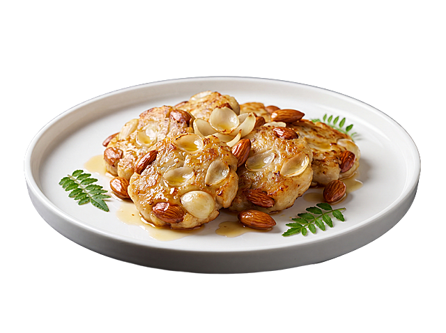 高清美食摄影作品，菜肴：百合杏仁煎鱼饼，盛放在白色陶瓷盘中，侧拍构图，纯哑光深灰黑色背景，柔和侧光打光突显食物立体感、油润光泽和丰富肌理，平视角度清晰展现菜品全貌，画面边缘点缀小型绿色蕨类植物叶片，极简风格，色彩对比强烈：菜品色泽鲜艳，餐具洁白，背景深沉，专业菜品摆盘，焦点锐利对准食物，浅景深使背景轻微虚化，酱汁呈现反光效果，配以质朴或精致的装饰，展现精致中式菜肴