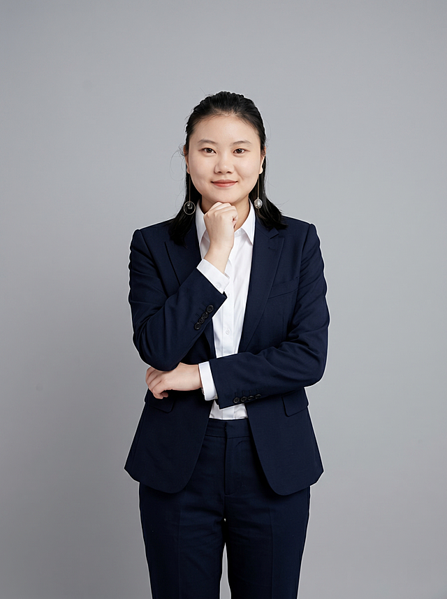 参考图中保留人物脸型、发型、年龄等特征生成教师咨询师职场全身形象照，标准焦段50mm，f/4光圈(f/2.8-f/4区间)，平视视角(镜头与人物视线齐平)；人物占画面70%，人物居中(居中构图)，位于画面中心，为视觉聚焦点，全身照，展现人物完整身形；左右留少量背景空间；头部与画面顶部保留5%空间；头部发型完整，头肩比例协调，人物结构准确；发质微微柔顺，微微蓬松。身穿藏青精纺羊毛混纺西装外套(平驳领设计，面料呈细腻微微哑光质感)；内搭白色高支精梳棉衬衫；下装藏青精纺羊毛混纺西裤；着装正式干练；亲和专业、耐心沉稳；身形匀称，姿态端正，身体挺拔。呈自然站姿，手扶下巴，肢体放松且自信；佩戴精致耳环，简约中性灰色纯色背景(呈现均匀柔和质感)，背景光线均匀柔和，强化色彩对比的高级感，极简干净；画质超高分辨率、细节清晰，现代精致感风格；肤质精细化处理；眼神直视镜头，目光坚定且澄澈，表情自然。嘴角上扬；清透自然裸妆(轻薄底妆+淡唇妆)妆感轻薄轻透裸肌感，通透感肤质，肤质自然细腻，肤色健康均匀，雾面柔光裸肌感，保留真实皮肤细节｡正面柔光补光，4800K中性光，面部光比1:1.5，色调明亮｡中近景写实摄影，对焦清晰，高清保留皮肤细节；分辨率4K，去除人物之外的所有元素。严格按照图片内容生成，发型保持不变，画面比例3:4