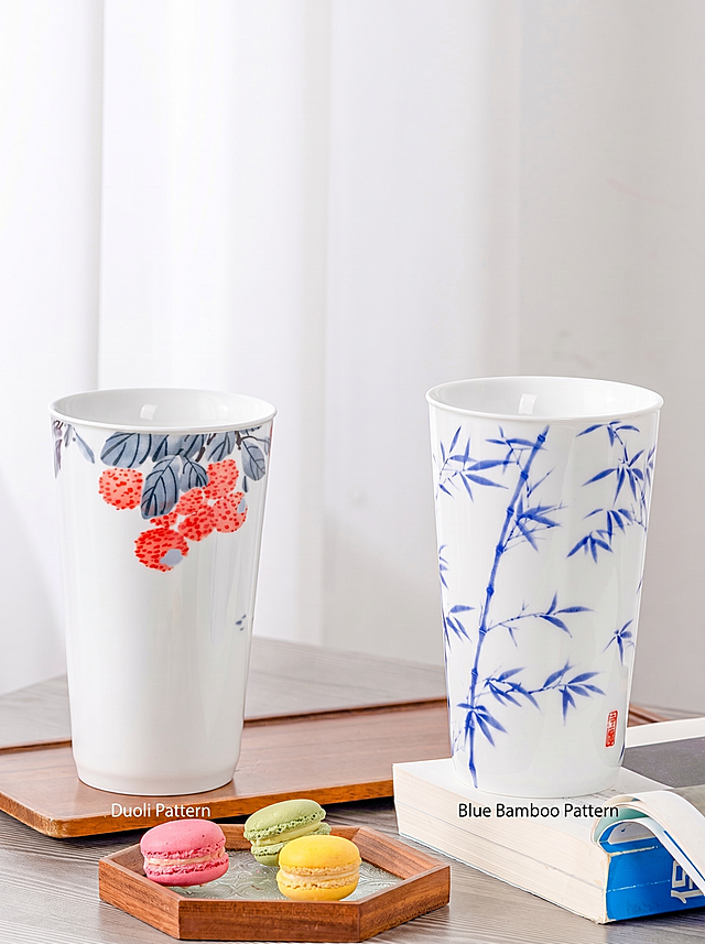 [主图-8] Multi-style SKU display. Clean combination display, clear product selection. Commercial still life photography, soft light, clear picture. Duoli pattern cup and blue bamboo pattern cup are placed together, the left Duoli cup (user's product) is the main focus, placed on a wooden tray, the right blue bamboo cup placed on a stacked book, three macarons in a hexagonal wooden plate in front for decoration. Keep the appearance and color of Duoli cup consistent with the input image, the two cups are placed naturally, the background is white wall with light gray. The picture is clean, the product is clearly visible. Soft natural light, the two cup glaze has a high light, the texture is real, the shadow is soft. Background light gray, wooden warm color, two cups of different patterns complement each other, rich color. Below each cup mark the corresponding style name "Duoli Pattern" / "Blue Bamboo Pattern", small font at the bottom, does not block the product. 3:4 ratio, 4k resolution, super high definition. Negative prompts: Deformation, text disorder, blurred product image, messy background, watermark, e-commerce platform Logo.