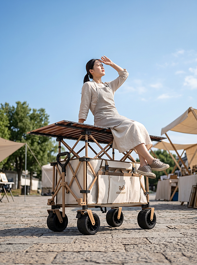 生成一张露营车摆摊的场景图，露营车完全采用提供的图片素材，不进行任何更改，包括角度。8K 超高清极致画质，佳能 5D4 相机，24mm 定焦镜头，f/2.8 大光圈，午后柔和通透自然光，写实商业实景摄影，物体超清肌理纹理，自然浅景深虚化，画面零畸变，画质干净通透，低角度仰拍，广角镜头。主体露营车：完全沿用参考图同款折叠露营车。人物：一个身形协调的东亚年轻女生，低马尾淡妆，简约棉麻长裙，前面围着摆摊穿的围裙，放松斜坐在推车木质桌板上，一只手向后撑住桌板支撑身体，一只手挡在额前遮阳光。穿了鞋的双脚自然垂落悬空。头部微微仰起看向上方，四肢舒展自然，肢体无畸形，神态慵懒温柔松弛。场景环境：户外文艺轻奢文创市集广场，复古石板路地面，空旷干净不杂乱，背景空旷，仰拍视角露出大片湛蓝天空，有云朵。远景全部柔焦虚化，不会抢画面主体。有明亮的阳光打在推车上，推车放置画面正中央，车身远离画面四边，画面上下左右预留大量空白留白区域，预留文字文案放置空间
