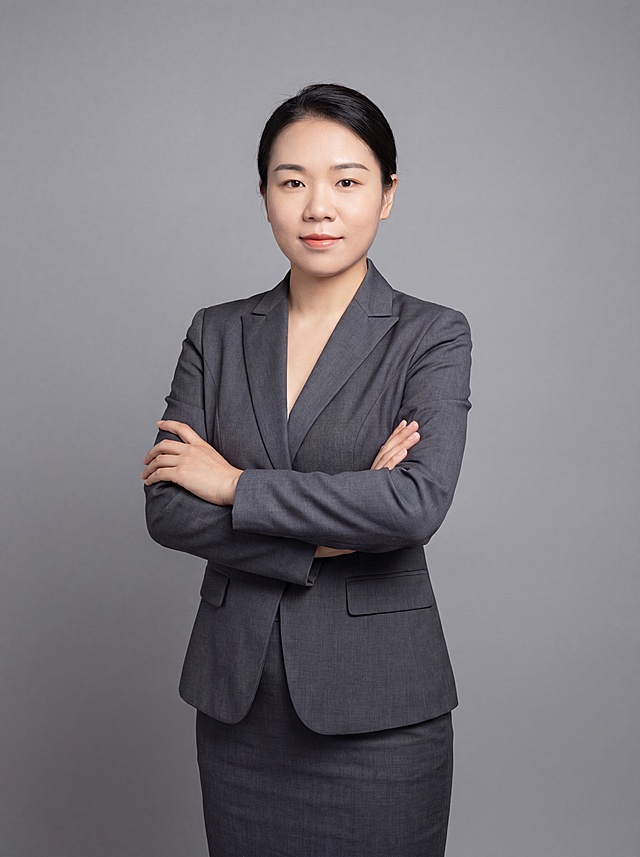 参考图中保留人物脸型、发型、年龄等特征生成职场形象照，标准焦段50mm，f/4光圈(f/2.8-f/4区间)，平视视角(镜头与人物视线齐平)；人物占画面70%，人物居中(居中构图)，位于画面中心，为视觉聚焦点，入境范围头部及以下至臀部下方10cm(半身像)；左右留少量背景空间；头部与画面顶部保留5%空间；头部发型完整，头肩比例协调，人物结构准确；身穿职业大女主西装裙装，面料呈细腻微微哑光质感；着装正式干练；专业稳重，气质从容果决；身形匀称，姿态端正，身体挺拔。呈双手抱胸的自然姿态，肢体放松且自信；发质微微柔顺，微微蓬松；简约中性灰色纯色背景(呈现均匀柔和质感)，背景光线均匀柔和，强化色彩对比的高级感。极简干净；画质超高分辨率、细节清晰，现代精致感风格；肤质精细化处理；眼神直视镜头，目光坚定且澄澈，表情自然。嘴角上扬；清透自然裸妆(轻薄底妆+淡唇妆)妆感轻薄轻透裸肌感，通透感肤质，肤质自然细腻，肤色健康均匀，雾面柔光裸肌感，保留真实皮肤细节｡正面柔光补光，4800K中性光，面部光比1:1.5，色调明亮｡中近景写实摄影，对焦清晰，高清保留皮肤细节；分辨率4K，去除人物之外的所有元素，去除所有配饰。严格按照图片内容生成，画面比例3:4