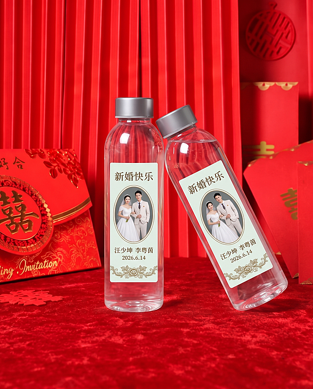 商业产品摄影，中式婚礼场景，红色丝绒台面，红色竖向褶皱背景布，左侧摆放印金色双喜的红色婚礼请柬，右侧散落几张带金色喜字的红卡纸；两个同款修长直筒透明水瓶，银灰色金属瓶盖，瓶身比例不变，左侧水瓶竖直稳稳站立，右侧水瓶倾斜倚靠在左侧瓶子的瓶肩，姿态完全参考参考图一；瓶内水体清澈通透，带有自然水光高光与折射，通透质感和普通矿泉水瓶一致；瓶身贴浅青白色竖版标签，标签顶部文字“新婚快乐”，中间椭圆形婚纱照（白纱新娘 + 浅西装新郎），下方文字“汪少坤 李粤茵 2026.6.14”，底部复古花卉装饰；柔和均匀室内柔光，红色喜庆氛围感，8K 超清，细节锐利，无底部白色文字，写实高清实拍质感