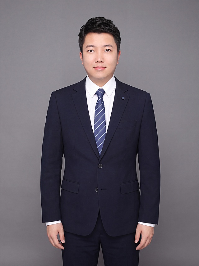 参考图中保留人物脸型、发型、年龄等特征生成职场全身职业形象照，标准焦段50mm，f/4光圈，平视视角，镜头与人物视线齐平，全身照，展现人物完整身形，人物占画面合适比例，人物居中，位于画面中心，为视觉聚焦点，左右留少量背景空间，头部与画面顶部保留合适空间，头身比例协调，人物结构准确。身穿深蓝色精纺羊毛混纺西装外套，平驳领设计，面料呈细腻微微哑光质感，内搭白色高支精梳棉衬衫，下装深蓝色精纺羊毛混纺西裤，系着蓝白条纹领带，佩戴精致胸针配饰，着装正式干练，专业稳重，身形匀称，姿态端正，身体挺拔。呈自然站姿，双手自然垂放，肢体放松且自信。发质微微柔顺，微微蓬松。简约微微中度灰色纯色背景，呈现均匀柔和质感，背景光线均匀柔和，强化色彩对比的高级感，极简干净。画质超高分辨率、细节清晰，现代精致感风格，肤质精细化处理，眼神直视镜头，目光坚定且澄澈，表情自然，嘴角上扬。肤质自然细腻，肤色健康均匀，皮肤状态清爽干净，保留真实皮肤细节。正面柔光补光，4800K中性光，面部光比1:1.5，写实摄影，对焦清晰，面部雾面柔光，轻透裸肌感，高清保留皮肤细节。分辨率4K，去除人物之外的所有元素，严格按照图片内容生成。画面比例3:4。