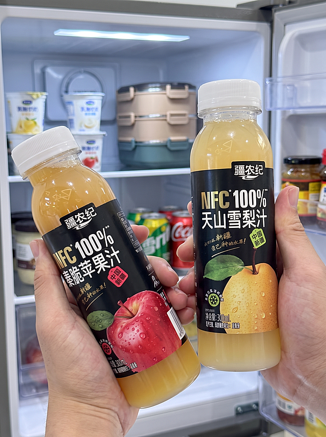 保留双手拿两瓶果汁构图，替换背景为办公室茶水间冰箱门打开场景，产品放在冰箱搁架上，保持产品和双手完整不变，所有文字清晰，尺寸比例3:4，均匀冷调冰箱灯光