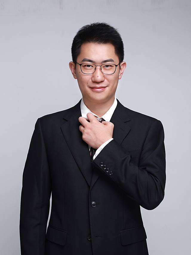 参考图中保留人物脸型、发型、年龄等特征生成职场形象照，标准焦段50mm，f/4光圈，平视视角，镜头与人物视线齐平；人物占画面70%，人物居中，居中构图，位于画面中心，为视觉聚焦点，入境范围头部及以下至臀部下方10cm（半身像）；左右留少量背景空间；头部与画面顶部保留5%空间；头部发型完整，头肩比例协调，人物结构准确；身穿深黑色精纺羊毛混纺西装外套，平驳领设计，面料呈细腻微微哑光质感；内搭白色高支精梳棉衬衫；下装深黑色精纺羊毛混纺西裤；着装正式干练；专业稳重；身形匀称，姿态端正，身体挺拔。呈手扶领带的自然姿态，肢体放松且自信；发质微微柔顺，微微蓬松；佩戴黑框眼镜；简约中性灰色纯色背景，呈现均匀柔和质感，背景光线均匀柔和，强化色彩对比的高级感，极简干净；画质超高分辨率、细节清晰，现代精致感风格；肤质精细化处理；眼神直视镜头，目光坚定且澄澈，表情自然。嘴角上扬；肤质自然细腻，肤色健康均匀，皮肤状态清爽干净，保留真实皮肤细节。正面柔光补光，4800K中性光，面部光比1:1.5。中近景写实摄影，对焦清晰，面部雾面柔光，轻透裸肌感，高清保留皮肤细节；分辨率4K，去除人物之外的所有多余元素。严格按照图片内容生成，保持清晰度，画面比例3:4