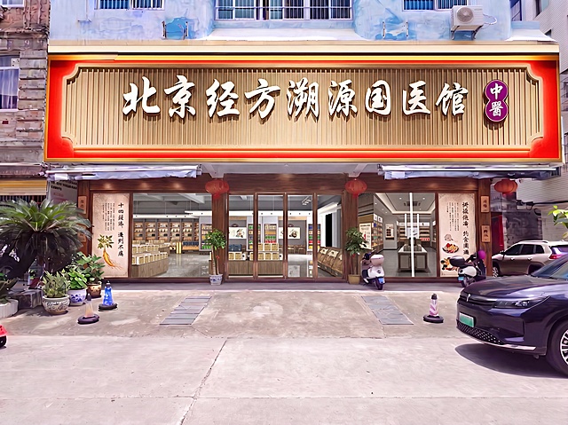 将图片2的门头替换为图片1的“北京经方溯源国医馆”门头样式，同时将大门也更换为图片1的玻璃大门样式，保留现有的两侧玻璃中医广告内容和周边环境，保持整体风格协调统一