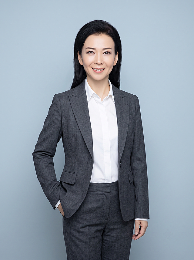 参考图中保留人物脸型、五官特征、发型、年龄生成全身职业装形象照，标准焦段50mm，f/4光圈，平视视角，人物居中，为视觉聚焦点，全身照，展现人物完整身形，左右留少量背景空间，头部与画面顶部保留5%空间，头肩比例协调，人物结构准确；身穿炭灰色精纺羊毛混纺西装外套，平驳领设计，面料呈细腻微微哑光质感；内搭白色高支精梳棉衬衫；下装炭灰色精纺羊毛混纺西装西裤；去除项链耳环戒指所有配饰，着装正式干练，专业稳重；身形匀称，姿态端正，身体挺拔。呈左手插兜的站姿，肢体放松且自信；发质微微柔顺，微微蓬松。简约冷灰蓝灰色纯色背景，呈现均匀柔和质感，背景光线均匀柔和，强化色彩对比的高级感，极简干净；画质超高分辨率、细节清晰，摄影棚级别，现代精致感风格；肤质精细化处理；眼神直视镜头，目光坚定且澄澈，表情自然，嘴角上扬；清透自然裸妆，轻薄底妆+淡唇妆，妆感轻薄轻透裸肌感，通透感肤质，肤质自然细腻，肤色健康均匀，雾面柔光裸肌感，保留真实皮肤细节。正面柔光补光，4800K中性光，面部光比1:1.5，色调明亮。写实摄影，对焦清晰，高清保留皮肤细节；分辨率4K，去除人物之外的所有元素。严格按照图片内容生成，不要改变人物五官。画面比例3:4