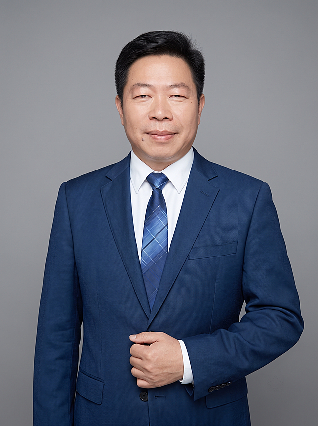 参考图中保留人物脸型、发型、年龄等特征生成企业高管职场形象照,标准焦段50mm,f/4光圈(f/2.8-f/4区间),平视视角(镜头与人物视线齐平);人物占画面70%,人物居中(居中构图),位于画面中心,为视觉聚焦点,入境范围头部及以下至臀部下方10cm(半身像);左右留少量背景空间;头部与画面顶部保留5%空间;头部发型完整,头肩比例协调,人物结构准确;发质微微柔顺，微微蓬松。身穿深蓝色精纺羊毛混纺西装外套,(平驳领设计,面料呈细腻微微哑光质感);内搭白色高支精梳棉衬衫;下装深蓝色精纺羊毛混纺西裤;系蓝色格纹真丝领带，着装正式干练;权威沉稳、格局开阔、从容果决、值得信赖;身形匀称,姿态端正,身体挺拔。呈自然站姿，右手轻握西装前襟，肢体放松且自信，去除胸针配饰。简约微微中度灰色纯色背景(呈现均匀柔和质感),背景光线均匀柔和,强化色彩对比的高级感。极简干净;画质超高分辨率、细节清晰,现代精致感风格;肤质精细化处理;眼神直视镜头,目光坚定且澄澈,表情自然。嘴角上扬;肤质自然细腻,肤色健康均匀,皮肤状态清爽干净,保留真实皮肤细节｡正面柔光补光,4800K中性光,面部光比1:1.5｡中近景写实摄影,对焦清晰,面部雾面柔光,轻透裸肌感,高清保留皮肤细节｡分辨率4K,去除人物之外的所有元素。严格按照图片内容生成。画面比例3:4