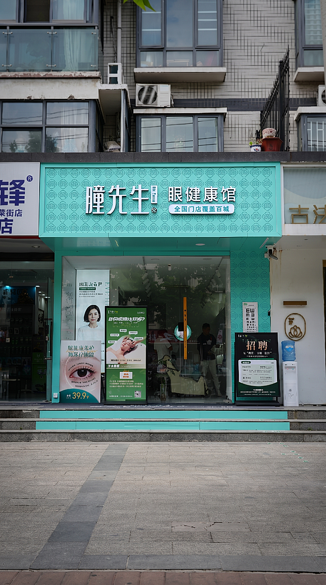 门头照片强化处理：突出‘瞳先生 眼健康馆’主招牌（青绿色底+白色立体字），其余相邻店铺（左侧‘锋荣街店’、右侧‘古法’等）做背景弱化处理——降低饱和度、轻微虚化、压暗对比度，使主店视觉焦点明确；保留街道地面与台阶细节，整体保持真实摄影风格，高清4K输出
