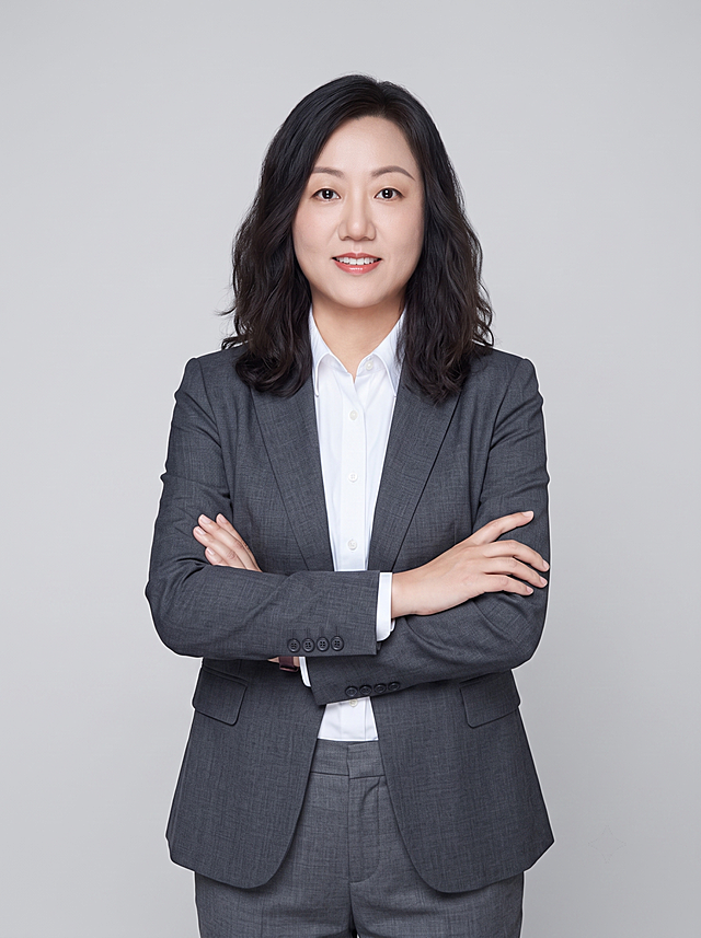 参考图中保留人物脸型、发型、年龄等特征生成律师职业形象照,标准焦段50mm,f/4光圈(f/2.8-f/4区间),平视视角(镜头与人物视线齐平);人物占画面70%,人物居中(居中构图),位于画面中心,为视觉聚焦点,入境范围头部及以下至臀部下方10cm(半身像);左右留少量背景空间;头部与画面顶部保留5%空间;头部发型完整,头肩比例协调,人物结构准确;身穿高级灰色精纺羊毛混纺西装外套,(平驳领设计,面料呈细腻微微哑光质感);内搭白色高支精梳棉衬衫;下装高级灰色精纺羊毛混纺直筒西装裤;着装正式干练;严谨理性、逻辑清晰、不怒自威、公信力强;身形匀称,姿态端正,身体挺拔。呈双手抱胸的自然站姿，肢体放松且自信;发质微微柔顺，微微蓬松。简约冷灰色纯色背景(呈现均匀柔和质感),背景光线均匀柔和,强化色彩对比的高级感。极简干净;画质超高分辨率、细节清晰,现代精致感风格;肤质精细化处理;眼神直视镜头,目光坚定且澄澈,表情自然。嘴角上扬;清透自然裸妆(轻薄底妆+淡唇妆)妆感轻薄轻透裸肌感,通透感肤质,肤质自然细腻,肤色健康均匀,雾面柔光裸肌感,保留真实皮肤细节。正面柔光补光,4800K中性光,面部光比1:1.5,色调明亮。中近景写实摄影,对焦清晰,高清保留皮肤细节。分辨率4K,去除人物之外的所有元素。严格按照图片内容生成。画面比例3:4