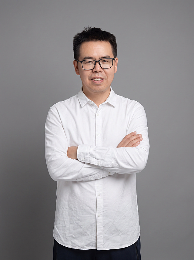 参考图中保留人物脸型、发型、年龄等特征生成职场形象照,标准焦段50mm,f/4光圈(f/2.8-f/4区间),平视视角(镜头与人物视线齐平);人物占画面70%,人物居中(居中构图),位于画面中心,为视觉聚焦点,入境范围头部及以下至臀部下方10cm(半身像);左右留少量背景空间;头部与画面顶部保留5%空间;头部发型完整,头肩比例协调,人物结构准确;身穿白色高支精梳棉长袖衬衫,(面料细腻挺括,微微哑光质感);下装深色西裤;着装正式干练;权威沉稳、从容果决、值得信赖;身形匀称,姿态端正,身体挺拔。呈站姿双手抱胸的自然姿态，肢体放松且自信;佩戴黑框眼镜;发质微微柔顺，微微蓬松。简约中性灰色纯色背景(呈现均匀柔和质感),背景光线均匀柔和,强化色彩对比的高级感,极简干净;画质超高分辨率、细节清晰,现代精致感风格;肤质精细化处理;眼神直视镜头,目光坚定且澄澈,表情自然。嘴角上扬;肤质自然细腻,肤色健康均匀,皮肤状态清爽干净,保留真实皮肤细节｡正面柔光补光,4800K中性光,面部光比1:1.5｡中近景写实摄影,对焦清晰,面部雾面柔光,轻透裸肌感,高清保留皮肤细节｡分辨率4K,去除人物之外的所有元素。严格按照图片内容生成。画面比例3:4
