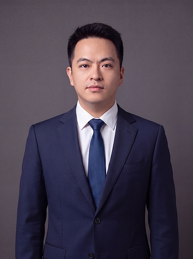 参考图中人物面部特征、脸型、发型、年龄完全保留不变，更换为藏青色纯色精纺羊毛西装，平驳领设计，面料细腻哑光质感，内搭白色高支精梳棉衬衫，系深蓝色商务领带，着装正式干练，沉稳大气；景别改为胸像照，取景到胸部以上位置，人物居中构图，头部与画面顶部保留5%空间，头肩比例协调，人物结构准确；姿态自然放松，肩膀舒展，眼神直视镜头，目光坚定，表情沉稳自然；深灰色纯色背景保持不变，背景光线均匀柔和；标准焦段50mm，f/4光圈，平视视角，镜头与人物视线齐平；画质超高分辨率、细节清晰，写实摄影，肤质自然细腻，肤色健康均匀，哑光肤质清爽干净，保留真实皮肤细节，面部光比1:1.5，4800K中性光，面部雾面柔光，轻透裸肌感，真实毛孔纹理；杰作，最佳画质，超高细节，中近景人像，柔光，正面补光，画面干净清新，高清皮肤细节，画面比例3:4