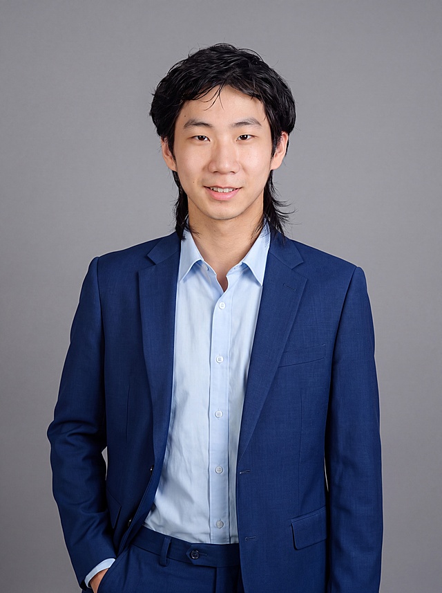 参考图中保留人物脸型、发型、年龄等特征生成职场形象照,标准焦段50mm,f/4光圈(f/2.8-f/4区间),平视视角(镜头与人物视线齐平);人物占画面70%,人物居中(居中构图),位于画面中心,为视觉聚焦点,入境范围头部及以下至臀部下方10cm(半身像);左右留少量背景空间;头部与画面顶部保留5%空间;头部发型完整,头肩比例协调,人物结构准确;身穿宝蓝色精纺羊毛混纺西装外套,(平驳领设计,面料呈细腻微微哑光质感);内搭浅蓝色高支精梳棉衬衫;下装宝蓝色精纺羊毛混纺西裤;着装正式干练;专业稳重;身形匀称,姿态端正,身体挺拔。呈自然站姿，左手插兜，肢体放松且自信;佩戴精致配饰;发质微微柔顺，微微蓬松。简约中性灰色纯色背景(呈现均匀柔和质感),背景光线均匀柔和,强化色彩对比的高级感。极简干净;画质超高分辨率、细节清晰,现代精致感风格;肤质精细化处理;眼神直视镜头,目光坚定且澄澈,表情自然。嘴角上扬;肤质自然细腻,肤色健康均匀,皮肤状态清爽干净,保留真实皮肤细节｡正面柔光补光,4800K中性光,面部光比1:1.5｡中近景写实摄影,对焦清晰,面部雾面柔光,轻透裸肌感,高清保留皮肤细节｡分辨率4K,去除人物之外的所有元素。严格按照图片内容生成。画面比例3:4
