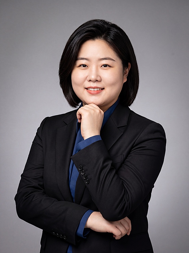 参考图中人物的脸型、发型、五官特征、年龄感完全保留，生成专业商务女性形象照。标准焦段50mm，f/4光圈，平视视角，镜头与人物视线齐平。人物占画面70%，居中构图，位于画面中心为视觉聚焦点，半身照，左右留少量背景空间，头部与画面顶部保留5%空间，头肩比例协调，人物结构准确。身穿深黑色精纺羊毛混纺西装套装，平驳领设计，面料呈细腻微微哑光质感；内搭深蓝色高支精梳棉上衣；下装为同材质同色西裤；着装正式干练，专业稳重，精英气质，身形匀称，姿态端正，身体挺拔。身体向右侧微转约30度，头部正对镜头，眼神专注，面带温和而自信的微笑。左臂自然地横在身前，右手肘搭在左手上，右手轻托下巴，肢体放松且自信。发型保持参考图中的黑色齐肩短发，发梢微微修整，干练大气，主体锐利。背景为专业摄影棚中性灰色纯色渐变背景，呈现均匀柔和质感，背景光线均匀柔和，强化色彩对比的高级感，极简干净。光线采用蝴蝶光与伦勃朗光结合，光线柔和明亮，面部立体感强，无杂乱阴影，面部光比1:1.5，4800K中性光，微微修饰脸型。超写实风格，照片画质高清，细节清晰，色调沉稳，整体呈现出专业、值得信赖的精英气质。肤质自然细腻，肤色健康均匀，哑光肤质清爽干净，保留真实皮肤细节，肤质哑光细腻，面部雾面柔光，轻透裸肌感，真实毛孔纹理。杰作，最佳画质，超高细节，写实摄影，中近景人像，皮肤质感自然清晰，柔光，正面补光，画面干净清新，高清皮肤细节。去除人物项链、耳环、包包、帽子等配饰。分辨率4K，严格按照参考图人物面部特征生成。