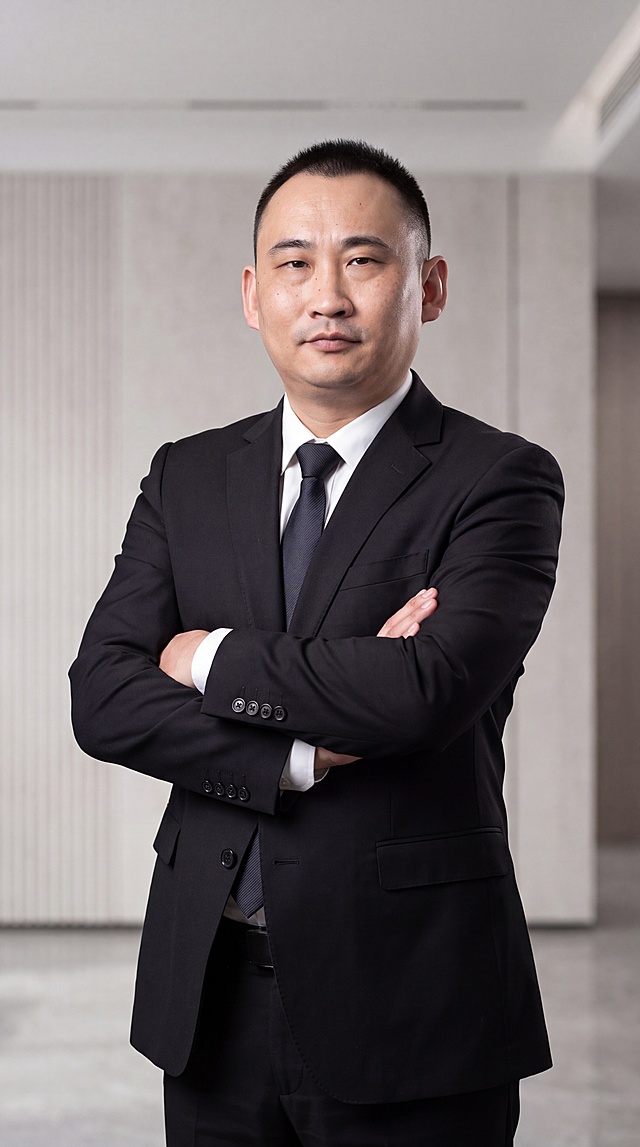 基于参考图中的男性本人形象，生成一张40岁男性商务形象照，全身到小腿位置，人物双手抱胸，高度还原本人面部特征，保留真实皮肤细节与纹理，身穿黑色西服套装，内搭衬衫，气质成熟干练，专业商务形象照风格，光线柔和均匀，背景简洁大气，超高清质感，细节丰富