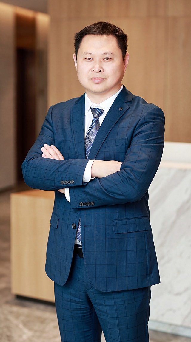 基于参考图中的男性本人形象，生成一张40岁男性商务形象照，全身到小腿位置，人物双手抱胸，高度还原本人面部特征和发型，保留真实皮肤细节与纹理，身穿深蓝色格纹西装套装，内搭白色衬衫和花纹领带，西装上保留胸针装饰，气质成熟干练，专业商务形象照风格，光线柔和均匀，背景简洁大气，超高清质感，细节丰富