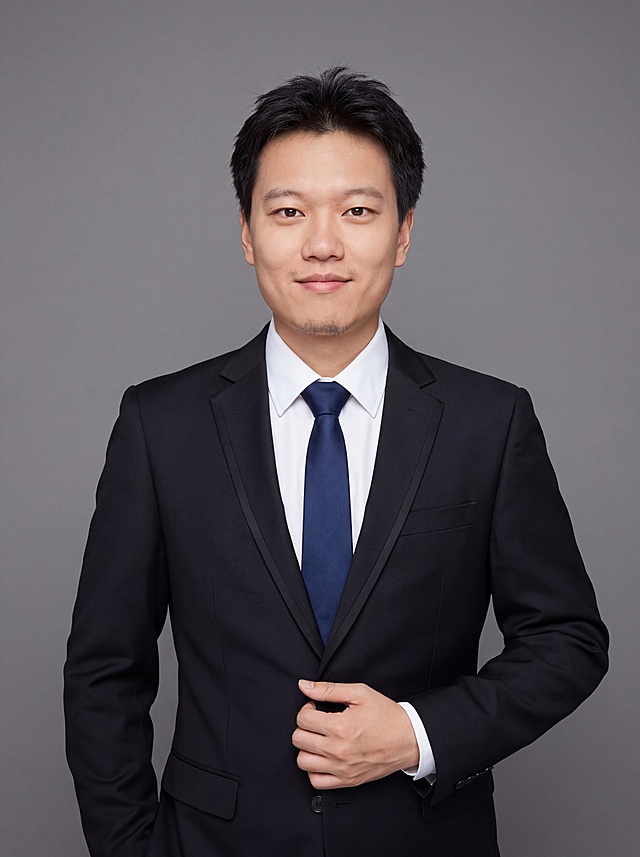 参考图中保留人物脸型、发型、年龄等特征生成职场正装形象照,标准焦段50mm,f/4光圈(f/2.8-f/4区间),平视视角(镜头与人物视线齐平);人物占画面70%,人物居中(居中构图),位于画面中心,为视觉聚焦点,入境范围头部及以下至臀部下方10cm(半身像);左右留少量背景空间;头部与画面顶部保留5%空间;头部发型完整,头肩比例协调,人物结构准确;身穿深黑色精纺羊毛混纺西装外套,(平驳领设计,面料呈细腻微微哑光质感);内搭白色高支精梳棉衬衫;系深蓝色真丝领带;下装深黑色精纺羊毛混纺西裤;着装正式干练;专业稳重、从容自信;身形匀称,姿态端正,身体挺拔。呈自然站姿，右手轻握西装前襟，肢体放松且自信;发质微微柔顺，微微蓬松。简约微微中度灰色纯色背景(呈现均匀柔和质感),背景光线均匀柔和,强化色彩对比的高级感。极简干净;画质超高分辨率、细节清晰,现代精致感风格;肤质精细化处理;眼神直视镜头,目光坚定且澄澈,表情自然。嘴角上扬;肤质自然细腻,肤色健康均匀,皮肤状态清爽干净,保留真实皮肤细节｡正面柔光补光,4800K中性光,面部光比1:1.5｡中近景写实摄影,对焦清晰,面部雾面柔光,轻透裸肌感,高清保留皮肤细节｡分辨率4K,去除人物之外的所有元素。严格按照图片内容生成。画面比例3:4