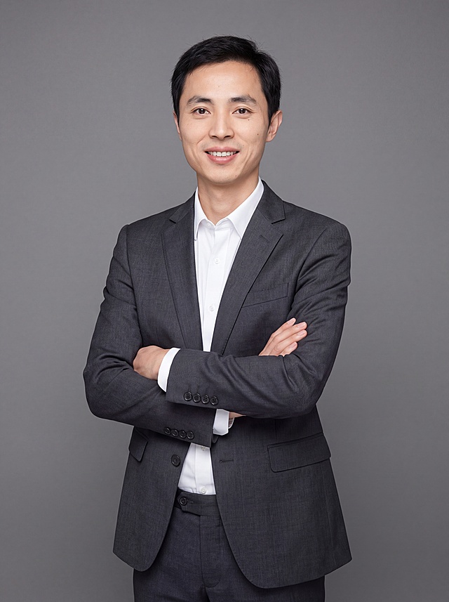参考图中保留人物脸型、发型、年龄等特征生成职场形象照,标准焦段50mm,f/4光圈(f/2.8-f/4区间),平视视角(镜头与人物视线齐平);人物占画面70%,人物居中(居中构图),位于画面中心,为视觉聚焦点,入境范围头部及以下至臀部下方10cm(半身像);左右留少量背景空间;头部与画面顶部保留5%空间;头部发型完整,头肩比例协调,人物结构准确;身穿深灰色精纺羊毛混纺西装外套,(平驳领设计,面料呈细腻微微哑光质感);内搭白色高支精梳棉衬衫;下装深灰色精纺羊毛混纺西裤;着装正式干练;专业稳重、从容自信;身形匀称,姿态端正,身体挺拔。呈站姿双手抱胸的自然姿态,肢体放松且自信;发质微微柔顺,微微蓬松。简约中性灰色纯色背景(呈现均匀柔和质感),背景光线均匀柔和,强化色彩对比的高级感,极简干净;画质超高分辨率、细节清晰,现代精致感风格;肤质精细化处理;眼神直视镜头,目光坚定且澄澈,表情自然。嘴角上扬;肤质自然细腻,肤色健康均匀,皮肤状态清爽干净,保留真实皮肤细节。正面柔光补光,4800K中性光,面部光比1:1.5。中近景写实摄影,对焦清晰,面部雾面柔光,轻透裸肌感,高清保留皮肤细节。分辨率4K,去除人物之外的所有元素。严格按照图片内容生成。画面比例3:4