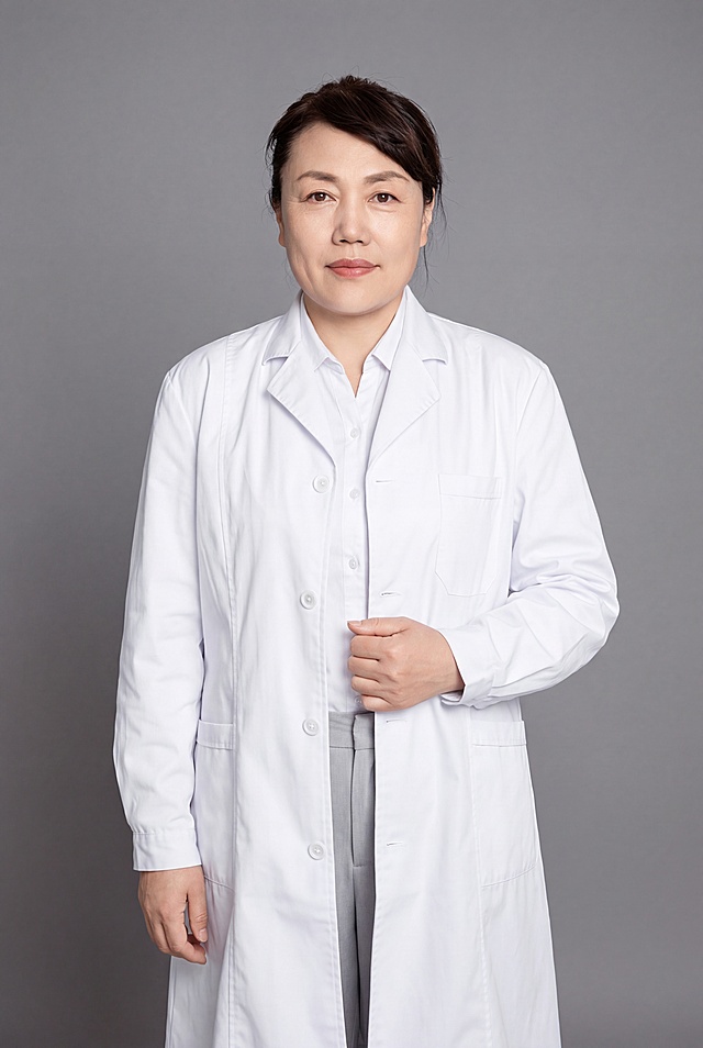 参考图中保留人物脸型、发型、年龄等面部特征生成医生职业全身形象照，标准焦段50mm，f/4光圈，平视视角，镜头与人物视线齐平；人物占画面约60%，人物居中构图，位于画面中心，为视觉聚焦点，全身照，展现人物完整身形；左右留少量背景空间；头部与画面顶部保留5%空间；头部发型完整，头肩比例协调，人物结构准确；身穿整洁白色白大褂，面料呈细腻微微哑光质感；内搭白色高支精梳棉衬衫；下装浅灰色西裤；着装正式干练；专业仁心、沉稳可靠、温和严谨；身形匀称，姿态端正，身体挺拔。呈自然站姿，右手轻握白大褂前襟，肢体放松且自信；发质微微柔顺，微微蓬松。简约微微中度灰色纯色背景，呈现均匀柔和质感，背景光线均匀柔和，强化色彩对比的高级感，极简干净；画质超高分辨率、细节清晰，现代精致感风格；肤质精细化处理；眼神直视镜头，目光坚定且澄澈，表情自然，嘴角微微上扬；清透自然裸妆，轻薄底妆+淡唇妆，妆感轻薄轻透裸肌感，通透感肤质，肤质自然细腻，肤色健康均匀，雾面柔光裸肌感，保留真实皮肤细节。正面柔光补光，4800K中性光，面部光比1:1.5，色调明亮。中近景写实摄影，对焦清晰，高清保留皮肤细节。分辨率4K，去除人物之外的所有元素，去除所有水印文字，严格按照图片内容生成，画面比例2:3