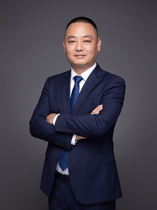 参考图1中人物的脸型、五官、发型、年龄等面部特征完全保留不变，生成专业商务形象照。参考图2的风格、姿势、构图和服装样式：身穿深藏青色精纺羊毛混纺西装外套，平驳领设计，面料呈细腻微微哑光质感；内搭白色高支精梳棉衬衫；系深蓝色真丝领带；下装同色同材质西裤。呈站姿，双臂交叉抱于胸前，肢体放松且自信，姿态端正，身体挺拔，专业稳重的气质。标准焦段50mm，f/4光圈，平视视角，镜头与人物视线齐平。人物占画面70%，人物居中构图，位于画面中心，为视觉聚焦点，半身照，入境范围头部及以下至臀部下方10cm。左右留少量背景空间，头部与画面顶部保留5%空间，头部发型完整，头肩比例协调，人物结构准确。发质微微柔顺，微微蓬松。深灰色纯色渐变背景，呈现均匀柔和质感，背景光线均匀柔和，强化色彩对比的高级感，极简干净。画质超高分辨率、细节清晰，现代精致感风格，肤质精细化处理。眼神直视镜头，目光坚定且澄澈，表情自然，嘴角微微上扬。肤质自然细腻，肤色健康均匀，皮肤状态清爽干净，保留真实皮肤细节。正面柔光补光，4800K中性光，面部光比1:1.5。中近景写实摄影，对焦清晰，面部雾面柔光，轻透裸肌感，高清保留皮肤细节。分辨率4K，去除人物之外的所有元素，严格按照图片内容生成。画面比例3:4。