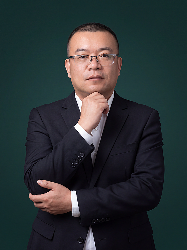 参考图1中人物的脸型、五官、年龄等面部特征，保留佩戴眼镜的特征，生成职场商务形象照。身穿深黑色精纺羊毛混纺西装外套，平驳领设计，面料呈细腻微微哑光质感；内搭白色高支精梳棉衬衫；下装深黑色精纺羊毛混纺西裤；着装正式干练，专业稳重，身形匀称，姿态端正，身体挺拔。呈站姿，右手手肘弯曲、右手轻扶下巴的姿态，左手自然交叠于身前，肢体放松且自信。发质微微柔顺，微微蓬松。深墨绿色渐变背景，呈现均匀柔和质感，背景光线均匀柔和，强化色彩对比的高级感，极简干净。画质超高分辨率、细节清晰，现代精致感风格；肤质精细化处理；眼神直视镜头，目光坚定且澄澈，表情自然沉稳。肤质自然细腻，肤色健康均匀，皮肤状态清爽干净，保留真实皮肤细节。正面柔光补光，4800K中性光，面部光比1:1.5。中近景写实摄影，对焦清晰，面部雾面柔光，轻透裸肌感，高清保留皮肤细节。标准焦段50mm，f/4光圈，平视视角，镜头与人物视线齐平；人物占画面70%，人物居中构图，位于画面中心，为视觉聚焦点，入境范围头部及以下至臀部下方10cm半身像；左右留少量背景空间；头部与画面顶部保留5%空间；头部发型完整，头肩比例协调，人物结构准确。分辨率4K，去除人物之外的所有元素，画面中不要出现二维码、文字等任何额外元素。严格按照图片内容生成。画面比例3:4。