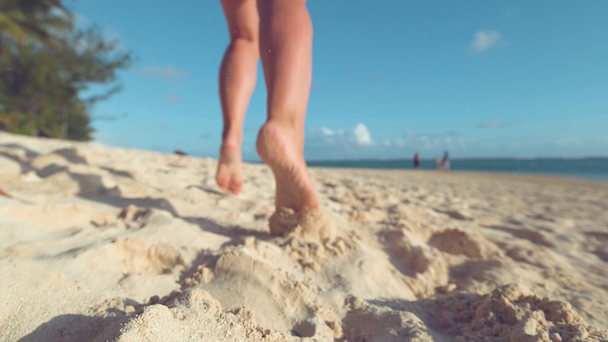 特写 当无法辨认的女子在沙滩上慢跑时，沙粒在空气中飞舞