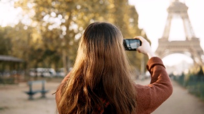 年轻女子在智能手机上拍照的后视图。十几岁的游客在法国巴黎探索埃菲尔铁塔