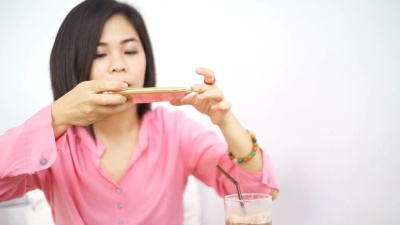 妇女用智能手机在木桌上用冰巧克力拍摄早餐照片。