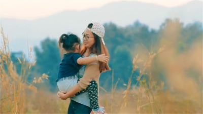 欢快的亚洲年轻母亲带着女儿一起在模糊的田野里