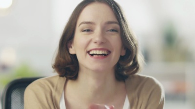 美丽的年轻女子对着镜头笑。她的背景是光明和模糊。
