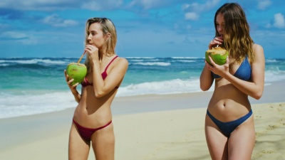 美丽的女孩喝着椰子在海滩上散步