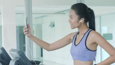 亚洲女孩在跑步机上跑步和打电话