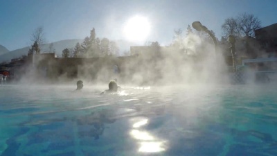 人们在冬季温泉浴池的天然热水中，在阳光的照射下，雪和水蒸气蒸发