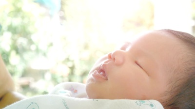 父母双手抱着新生儿的特写镜头，婴儿睡在她的手臂上。无噪音家庭无忧无虑的幸福家庭愿望概念